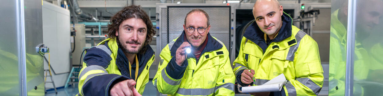 3 inspecteurs van de ANVS poseren in een hal van nucleaire installaties Urenco.